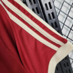 Close-up of a red athletic jersey sleeve with white double piping on a cream trim, hanging on a metal rack.