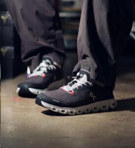 Close-up of black athletic running shoes with white laces on a person standing on a concrete floor.