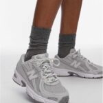 Person wearing gray crew socks and light gray athletic sneakers, standing with one foot forward.