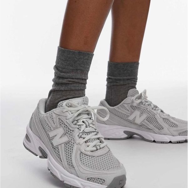 Person wearing gray crew socks and light gray athletic sneakers, standing with one foot forward.