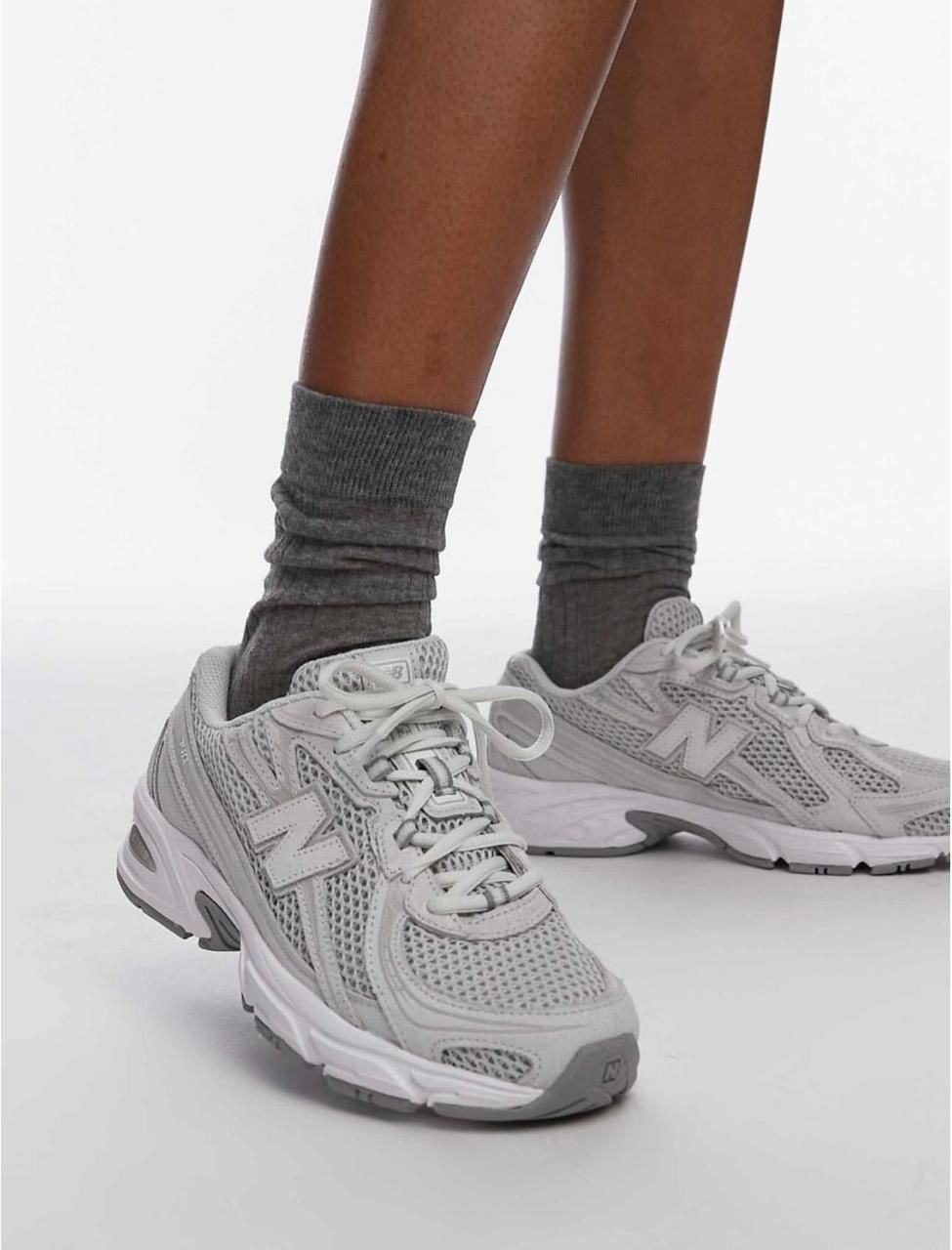 8fec9ec4-77b8-4758-ae19-9252f1b9eefe Person wearing gray crew socks and light gray athletic sneakers, standing with one foot forward.