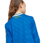 Person viewed from behind wearing a blue sports jersey; yellow 'RMCF' lettering at the neck on the back collar area