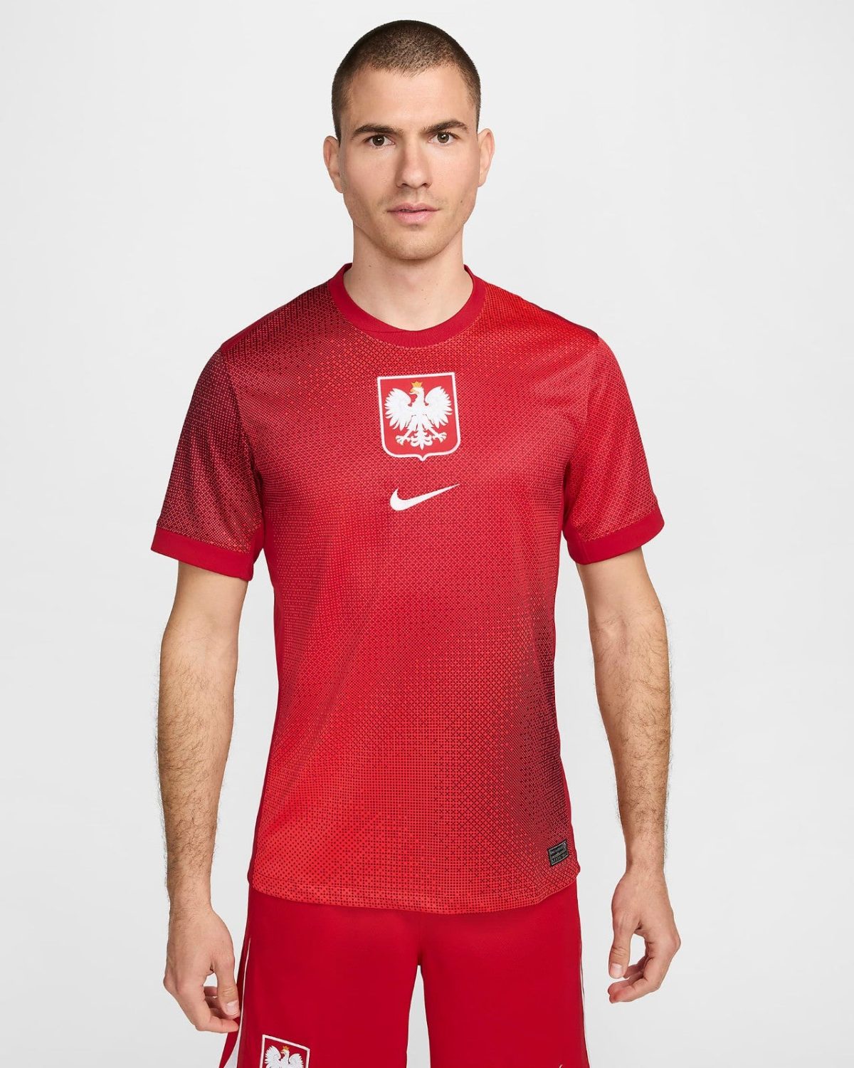 Man wearing a red Poland national team soccer jersey with white eagle crest and Nike logo, facing camera in a studio.