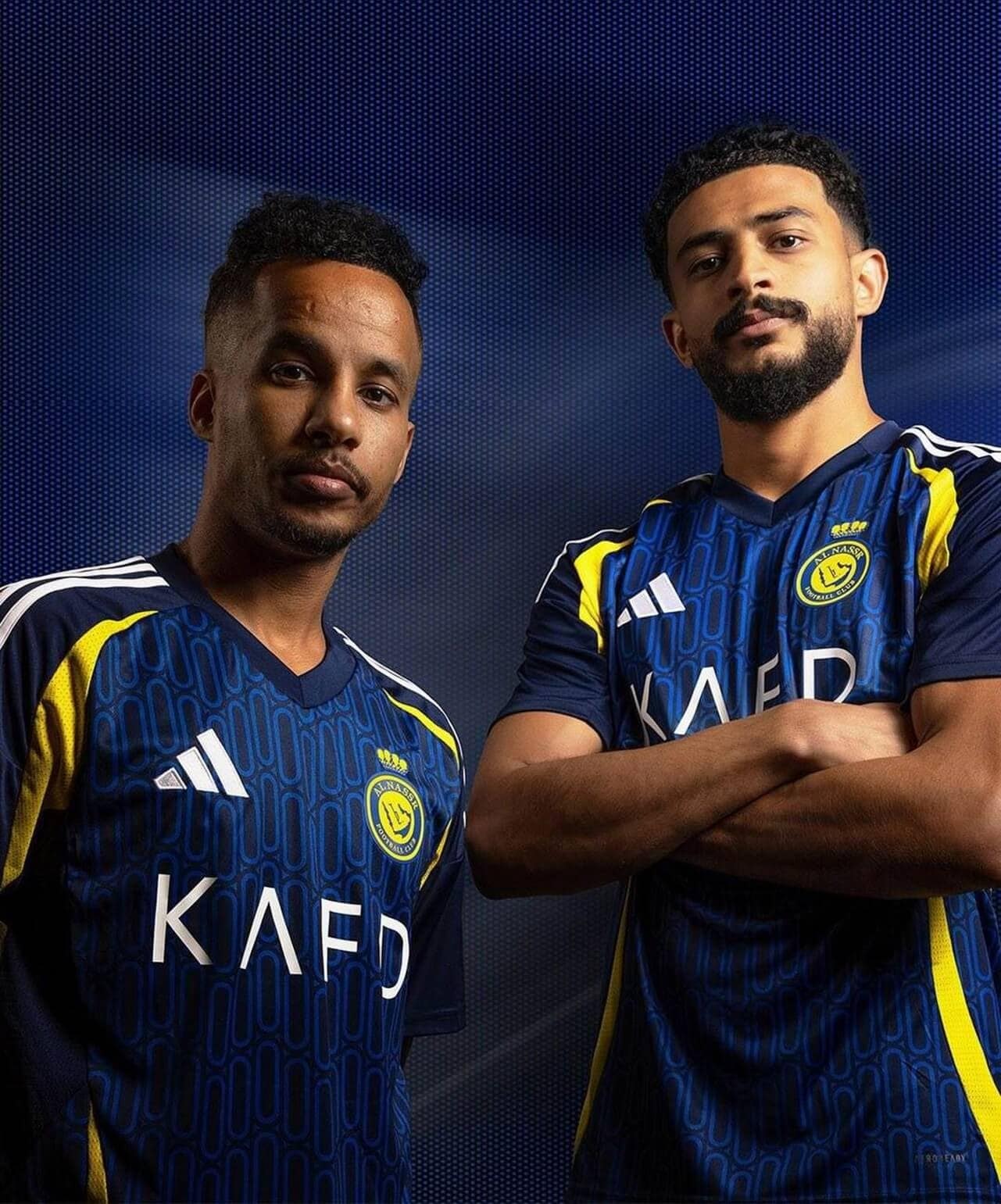 8pUdp7zeVz1ZJJR | UAE SPORT STORE Two young men in matching blue athletic jerseys pose confidently against a dark, dotted blue background, arms folded.
