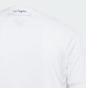 8wjqJ9goiuSABUR | UAE SPORT STORE Close-up of a white shirt shoulder with blue 'Los Angeles' script on the collar edge.