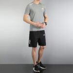 Person wearing a gray Adidas athletic T-shirt and black Adidas shorts with white logos, standing in a neutral pose in a studio look.