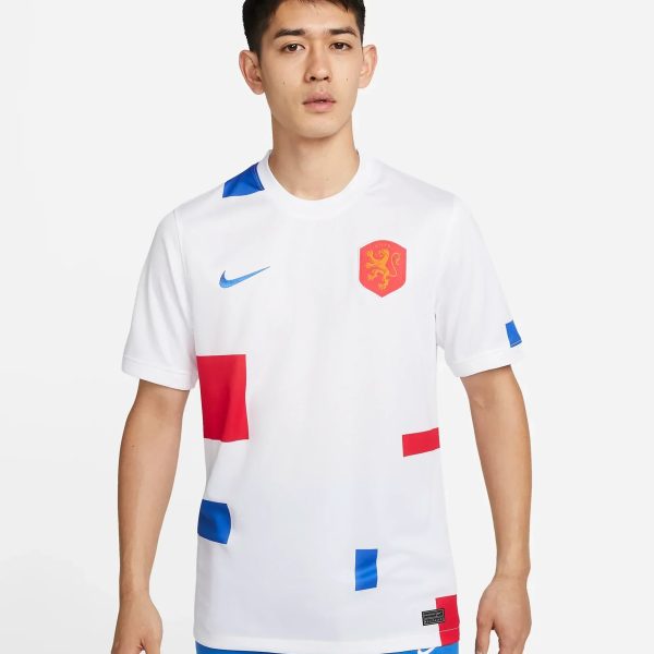 Young man modeling a white soccer jersey with blue accents and a red crest featuring a yellow lion on the chest, against a light background.