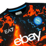 Close-up of a black patterned jersey with the white 'ebay' logo, 'EA7' text, and a blue circular badge with an 'N'