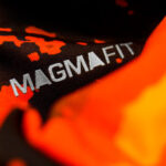Close-up of black fabric with the white text 'MAGMA FIT' and orange-red accents, suggesting branded athletic gear.