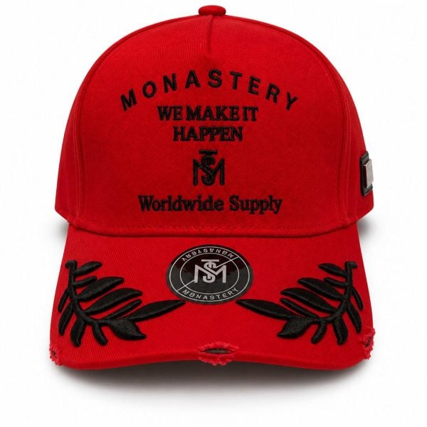 Red baseball cap with black embroidery reading 'MONASTERY WE MAKE IT HAPPEN Worldwide Supply' and floral leaf accents on the brim.