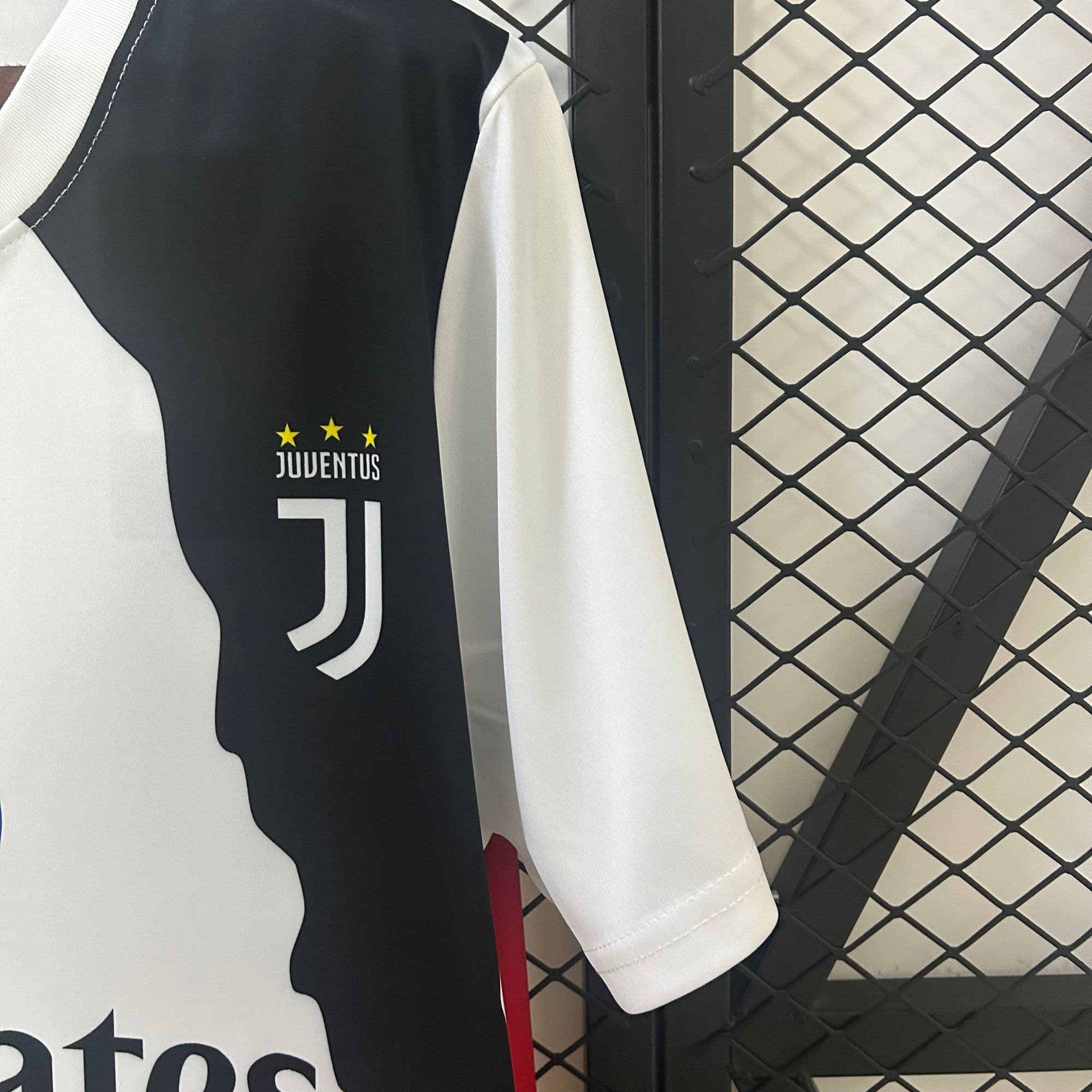 918b9458 | UAE SPORT STORE Juventus football jersey hanging on a rack, black and white panels with three yellow stars above 'JUVENTUS' text.