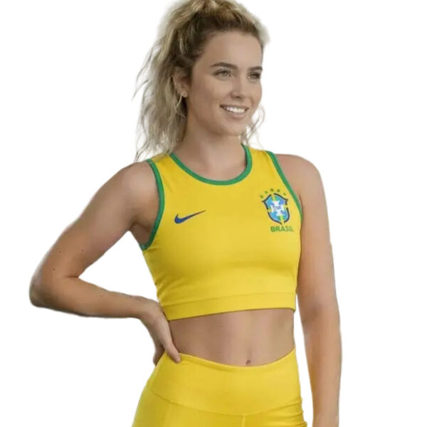 Young woman in yellow Brazil sports top and shorts, smiling with hand on hip; athletic pose; crest and Nike logo visible on jersey.