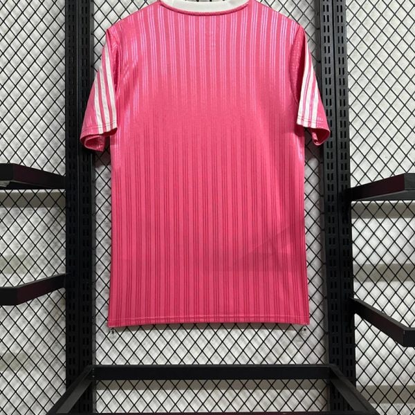 Bright pink striped T-shirt on a wooden hanger against a black grid display in a store windowed rack, showing vertical stripe pattern and white collar.