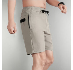 91ab6daf | UAE SPORT STORE Man wearing beige knee-length shorts with a black drawstring and zippered side pocket on the left leg.