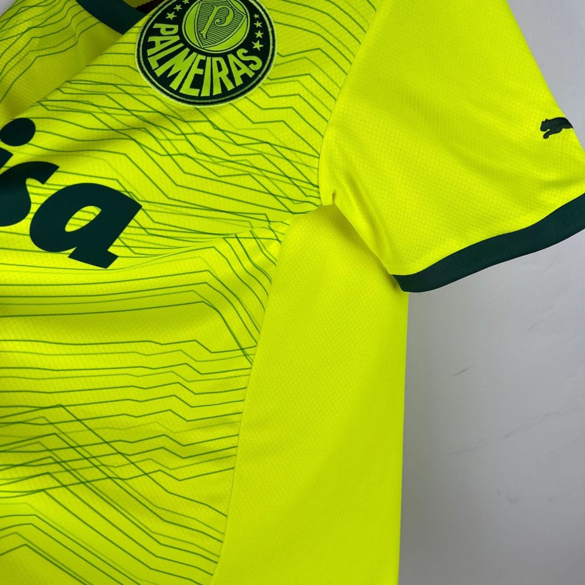 Close-up of a neon yellow high-visibility sports jersey showing a circular team badge and a Puma logo nearby.