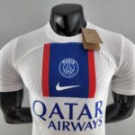 Mannequin wearing a white Paris Saint‑Germain jersey with blue and red stripes and a brown tag attached to the collar area, front view.