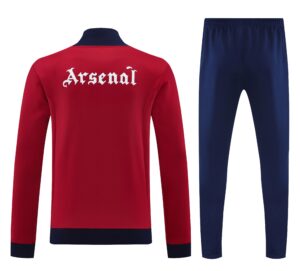 921e6dfe | UAE SPORT STORE Red sports jacket viewed from the back with the word 'Arsenal' in white Gothic font, paired with navy jogger pants in the background.