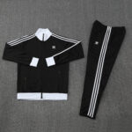 Black Adidas tracksuit jacket and matching pants with white stripes, laid flat on a gray surface.