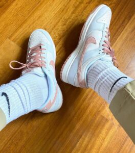 Pastel blue and pink Nike sneakers on feet, white socks, standing on a wooden floor.
