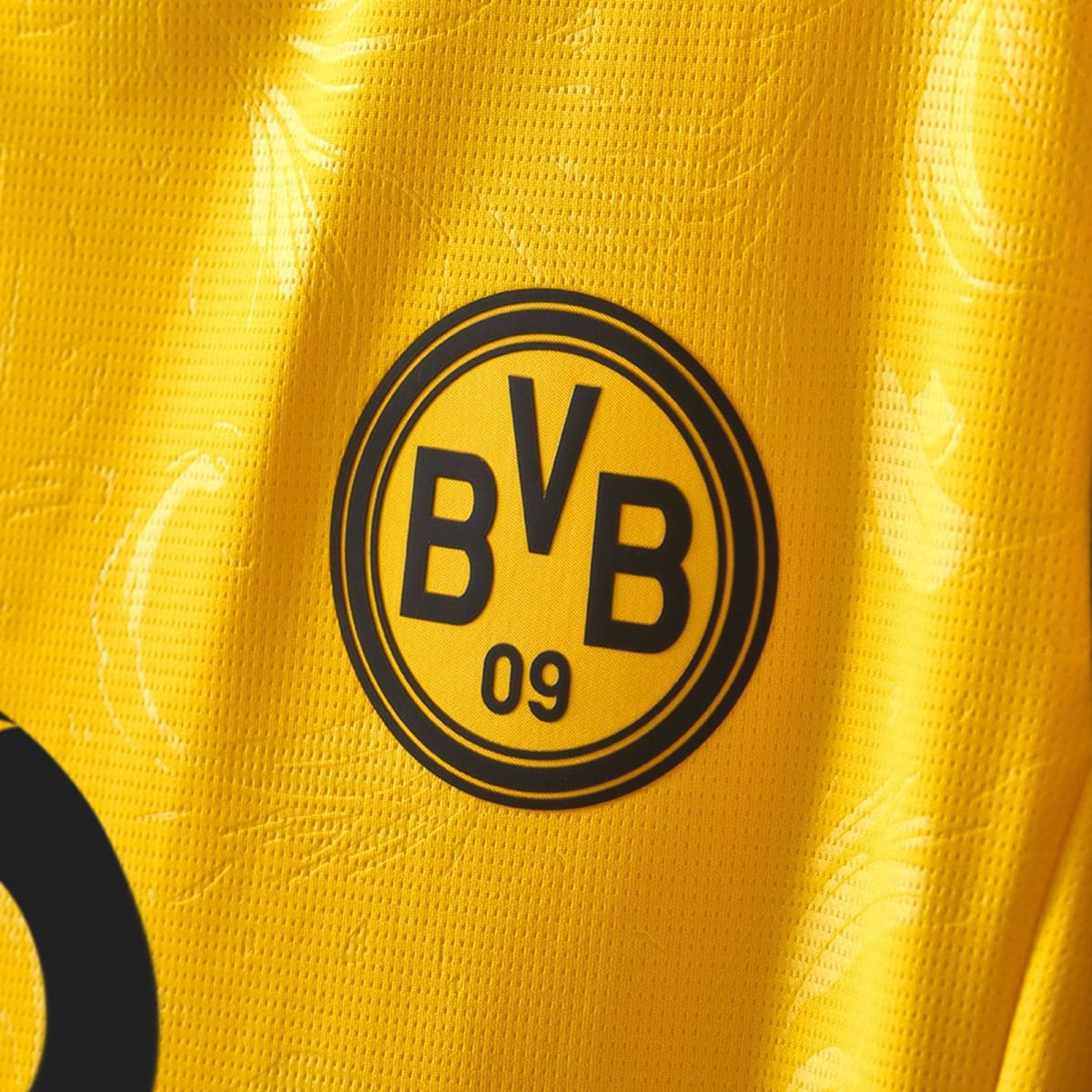 Close-up of a yellow Borussia Dortmund jersey fabric with the BVB badge visible reading 'BVB 09'.