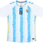 Light blue football/soccer jersey with yellow trim, featuring a Malaga CF crest on the chest and Hummel logos, with product tags attached.