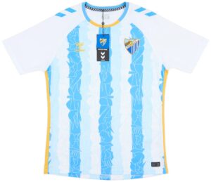 Light blue football/soccer jersey with yellow trim, featuring a Malaga CF crest on the chest and Hummel logos, with product tags attached.