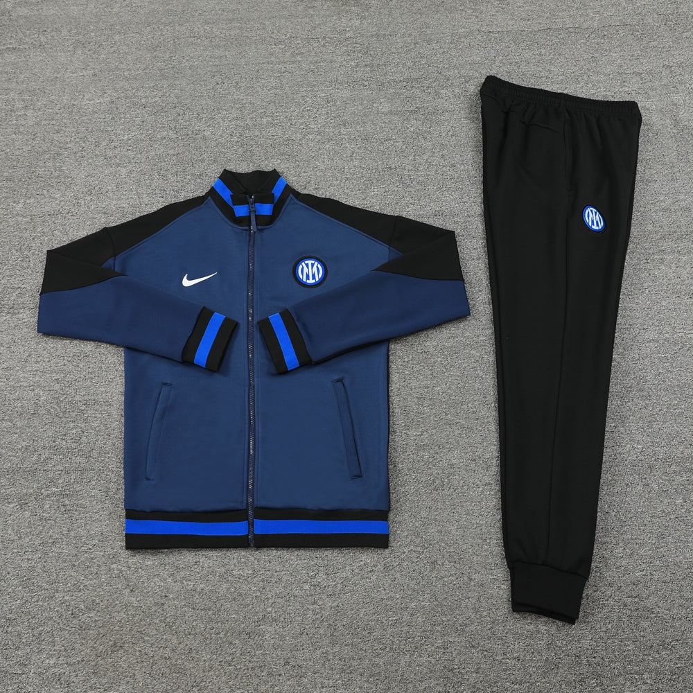 92c09719 | UAE SPORT STORE Blue and black Inter Milan track suit (zip jacket and matching pants) laid flat on a gray carpet; jacket features a white Nike swoosh and Inter crest, with blue and black color blocks and striped cuffs, pants have an Inter crest.
