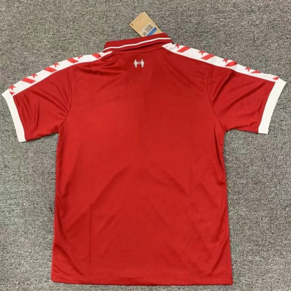 Back view of a red polo shirt laid flat on a gray carpet, white stripes along the shoulders and white sleeve cuffs, tag at the collar.
