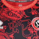 Close-up of a red and black sports jersey with a dragon motif, gold geometric collar trim, and a circular Sheffield crest.