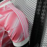 93afbfa9-4d3f-45e0-8ccf-63bf6f0d03b8 | UAE SPORT STORE Close-up of a pink sports jersey sleeve with white stripes, against a chain-link fence background.