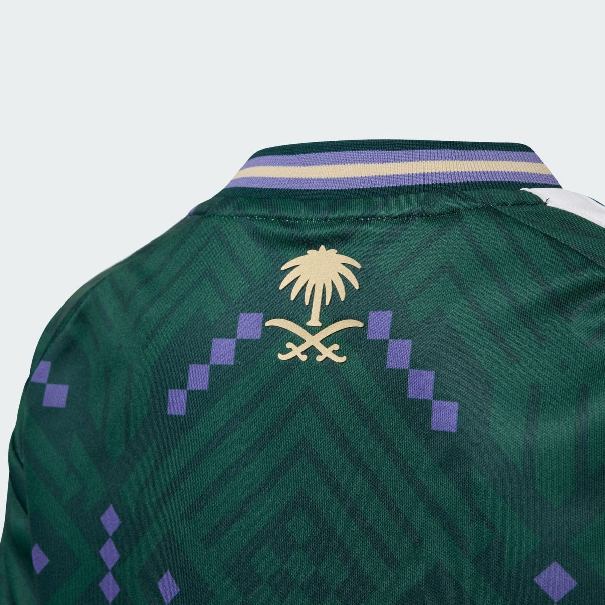 Close-up of a green jacket collar area featuring a gold palm tree emblem and purple geometric squares on a dark green fabric.