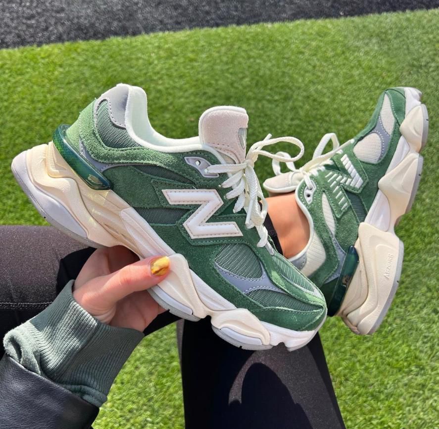 94206d48-1395-49b2-9518-3103b1f20f46 Green New Balance sneakers with white accents being held against a grass field backdrop.