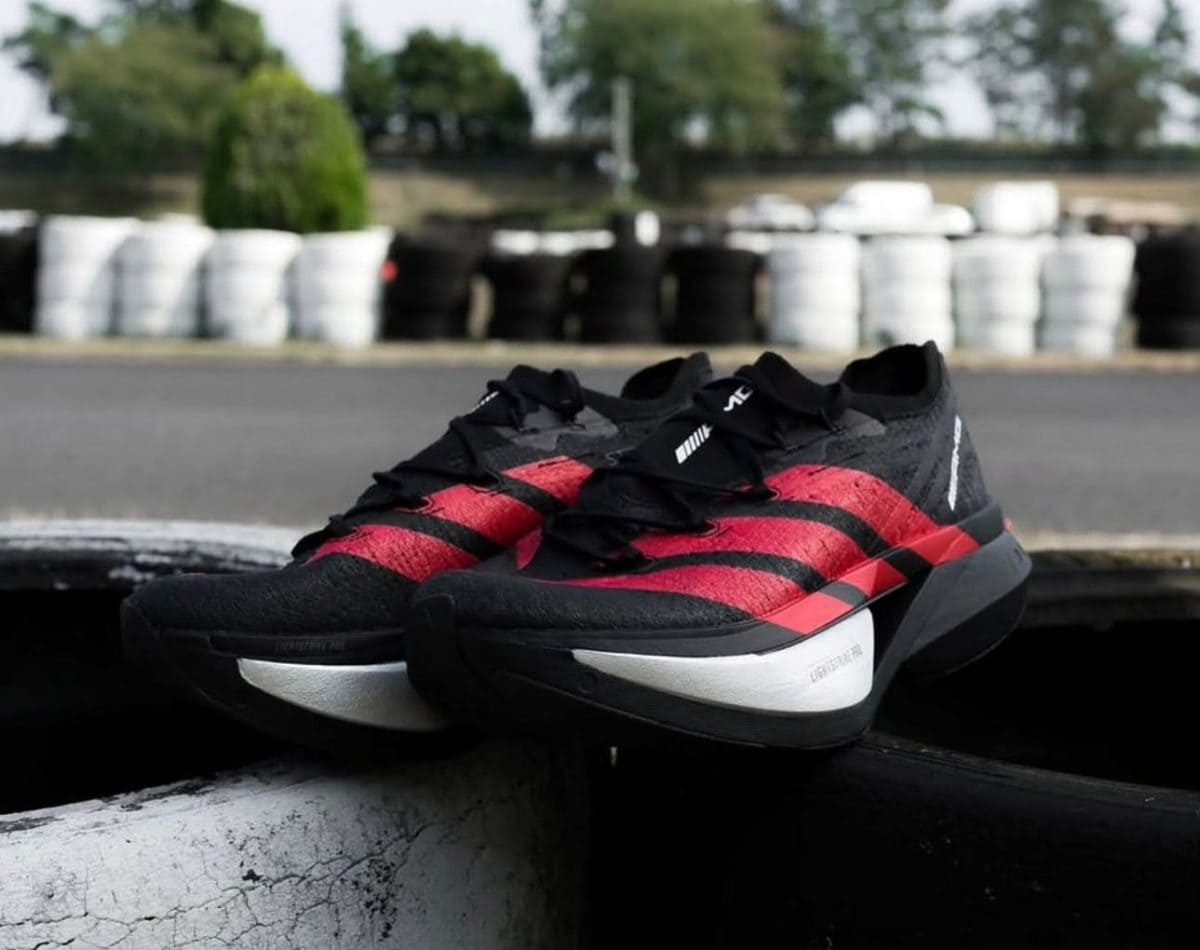 Pair of black and red running shoes resting on a ledge near a race track with stacked tires in the background