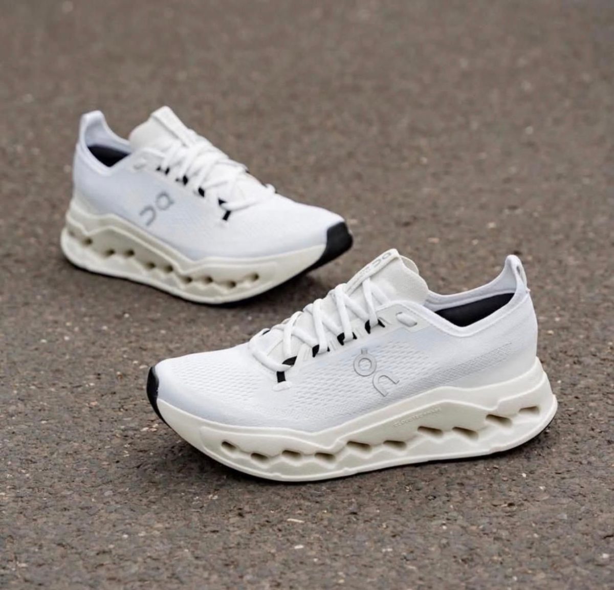 Pair of white running shoes with chunky, wavy cream soles resting on pavement.