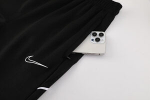 Black athletic pants with white Nike swoosh and a silver smartphone peeking from the pocket behind the logo.