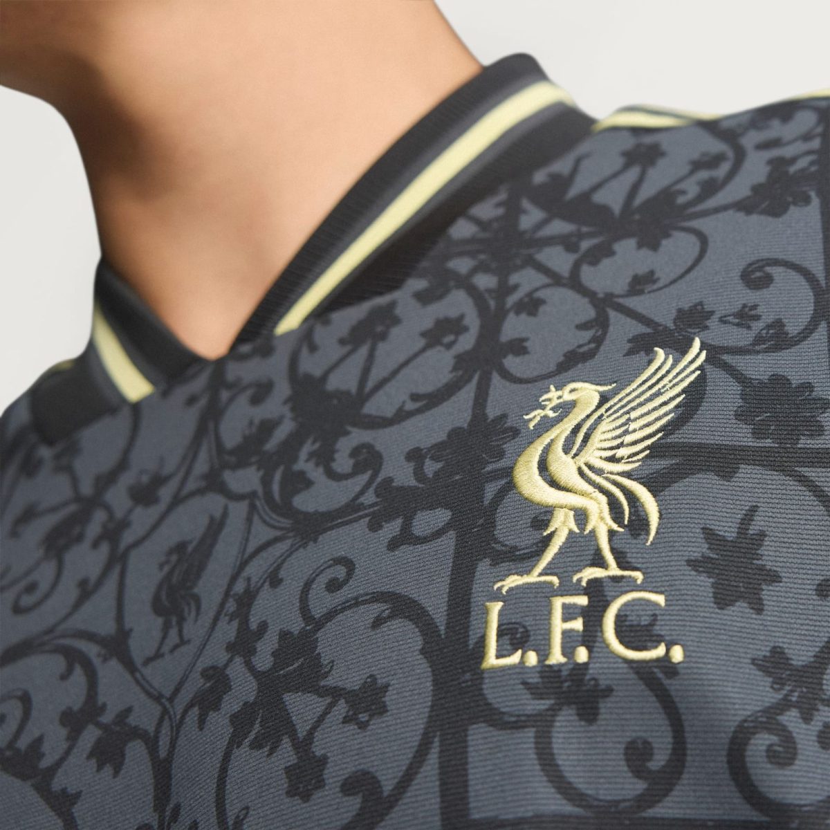 Close-up of a dark patterned polo shirt collar with gold embroidery of a bird and L.F.C. initials.