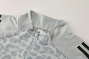 Close-up of a light gray zip-front jacket with a patterned fabric and high collar. The zipper is centered, showing a pale mint zipper pull.