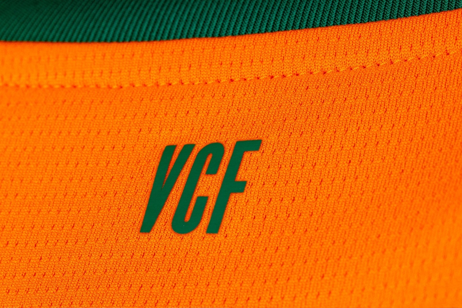 96CafFqIbSHmZsK | UAE SPORT STORE Close-up of bright orange fabric with a teal 'VGF' logo stitched on it.