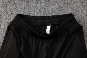 Close-up of black athletic shorts waistband with elastic, size tag showing S visible on gray carpet