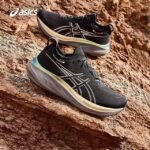 Black ASICS running shoes with cream-to-tan soles resting on a rugged red rock surface outdoors.