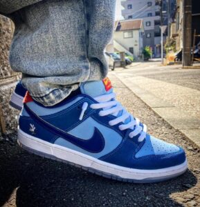 Close-up of a blue Nike sneaker with white laces on a sidewalk, denim pants cuffed at the ankle.