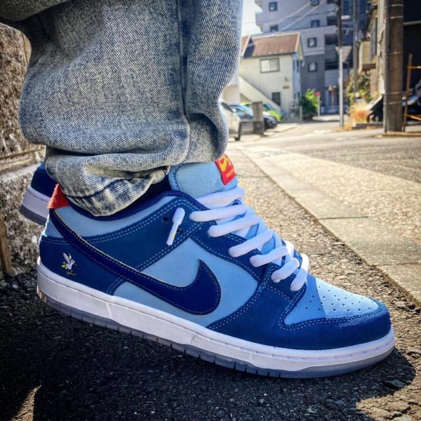 Close-up of a blue Nike sneaker with white laces on a sidewalk, denim pants cuffed at the ankle.