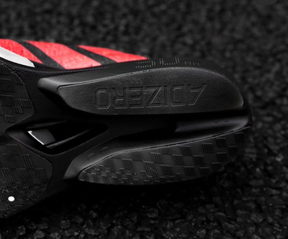 Close-up of a black running shoe outsole with red accents, featuring the embossed word 'ADIZERO'.