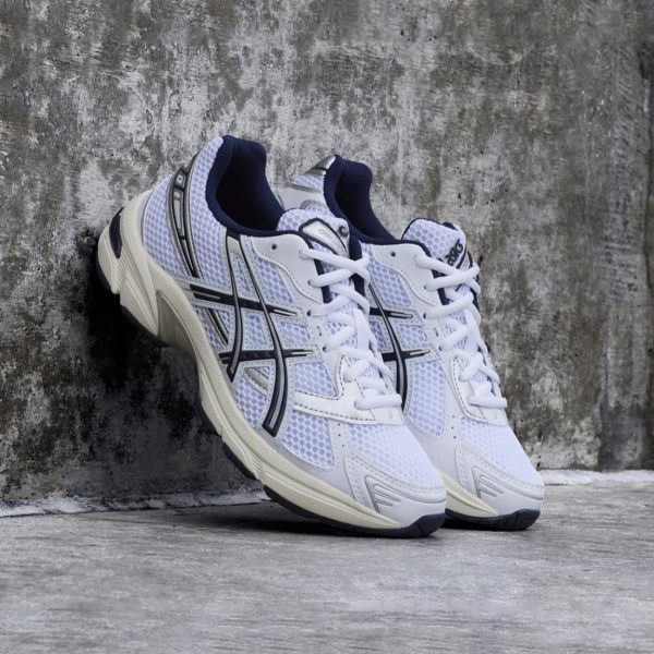 98533215-d409-45c2-9caf-105c95d3e11b | UAE SPORT STORE Pair of white and navy ASICS running shoes with mesh panels leaning against a textured concrete wall.