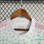 White athletic-style shirt with mint green spots and pink shoulder stripes hanging on a wooden hanger.