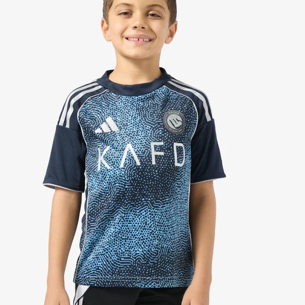 Smiling boy wearing a blue patterned soccer jersey and black shorts, standing against a light background.