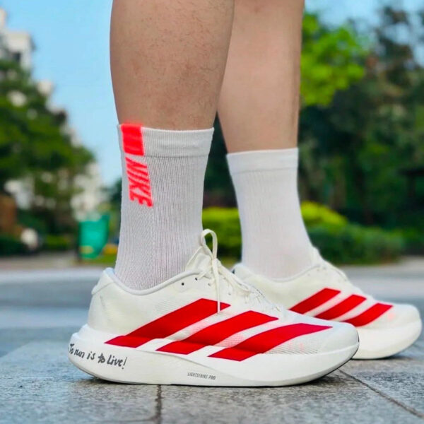 Person standing outdoors in white running shoes with red stripes and white socks; the shoe sole reads “To run is to Live!”