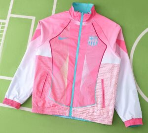 Pink Barcelona windbreaker with teal zipper and crest on the left chest, white sleeves, and geometric teal accents against a green background.