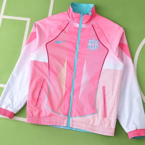 Pink Barcelona windbreaker with teal zipper and crest on the left chest, white sleeves, and geometric teal accents against a green background.