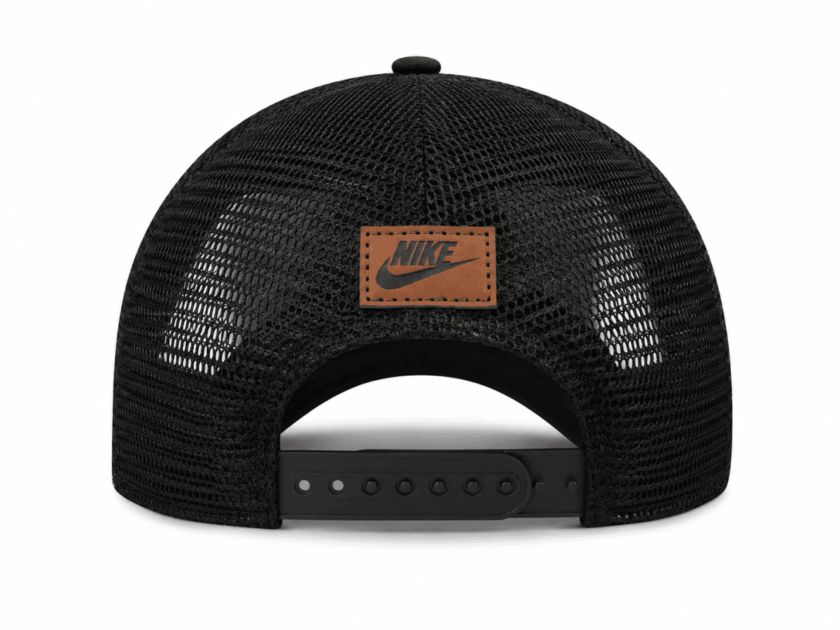 Back view of a black Nike mesh trucker cap with an adjustable snap strap and brown leather logo patch on the back panel.